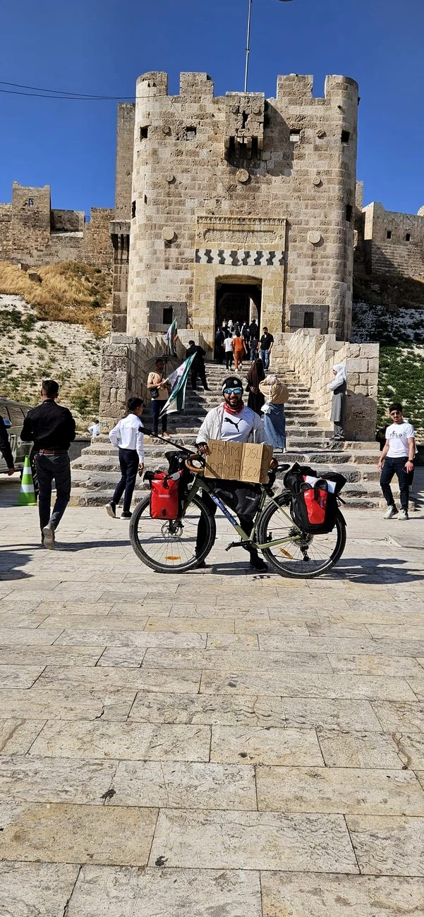 Touring cyclist with loaded bicycle in front of a historic citadel