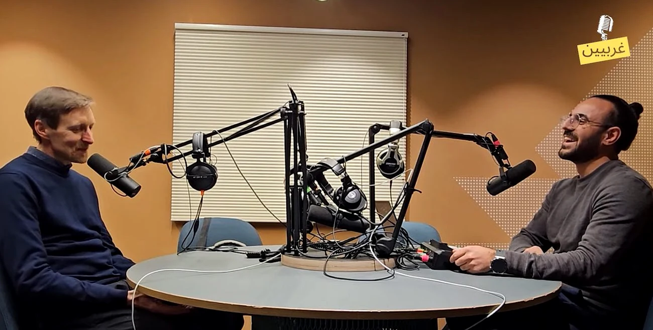 Two podcast participants seated across a studio table